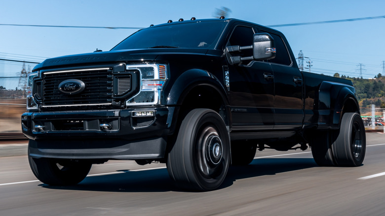 A black heavy-duty Ford pickup truck driving down a road with blue skies in the background.
