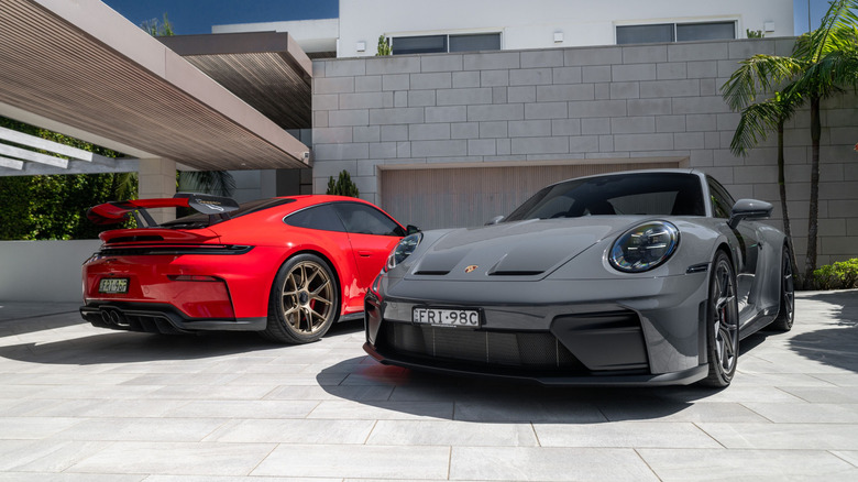 A red 2026 Porsche 911 GT3 and a gray 2026 Porsche 911 GT3 Touring parked in a driveway.