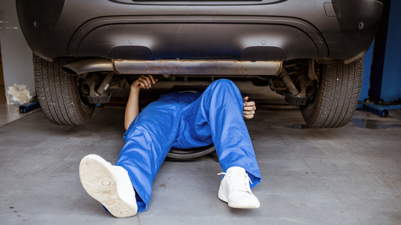 A pair of legs of an individual under a car, fixing it.