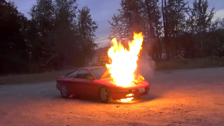 A '90s Ford Probe with a front end that's engulfed in flames.