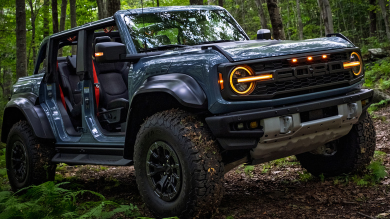 Ford Bronco Raptor off-roading in a forest with its doors removed.