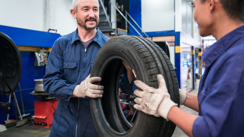 Technicians at a tire shop holding a new tire for the customer