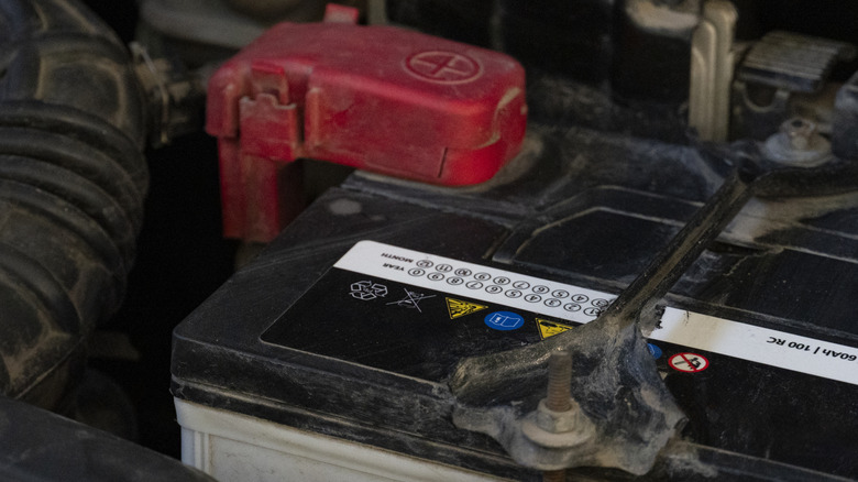 The top of a car battery, with its red positive terminal cover in the background.
