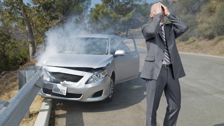 Man standing next to silver sedan after crashing into guardrail