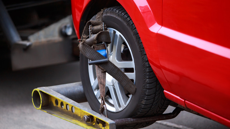 The front wheels of a car safely strapped to a tow truck's tow bar lift.