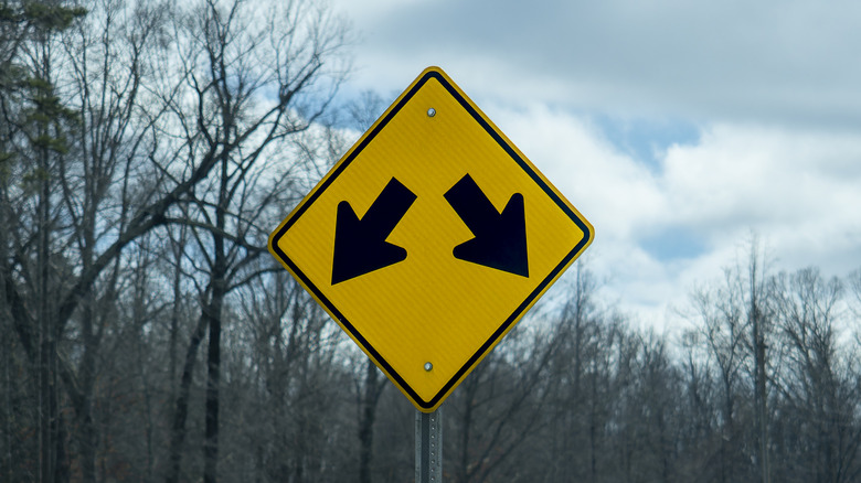 A yellow road sign with two arrows pointing down, indicating the lanes split away from each other.