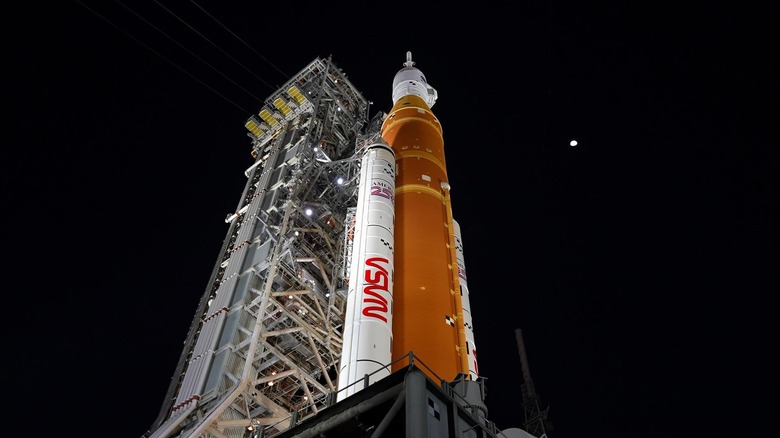 Underview of the Artemis II rocket on the launchpad, with the Moon behind