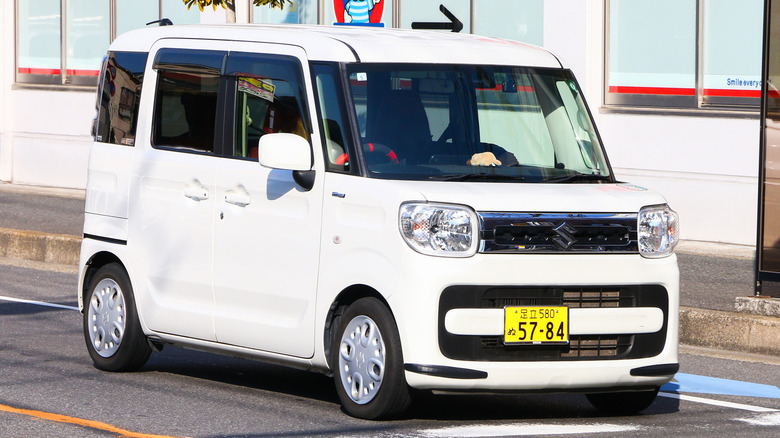 A white Dacia kei car sitting at a traffic light.