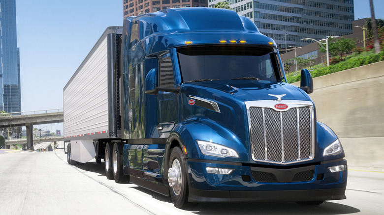 A 2025 Peterbilt 379 with blue cab and white sides driving down a highway in a city