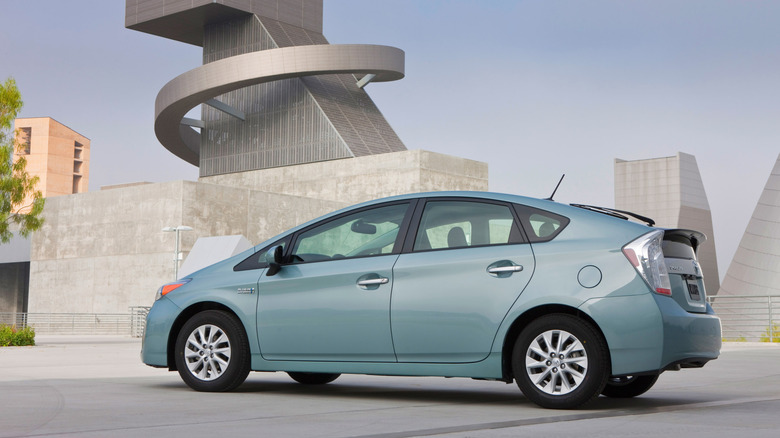 A light teal blue-green first generation Toyota Prius on a parking garage with a modern building in the background.