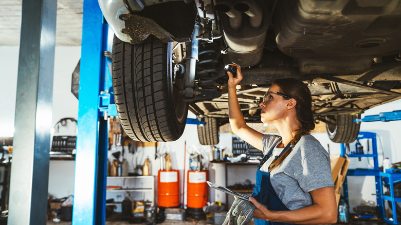 A young mechanic looking at a car's underbody on a lift.