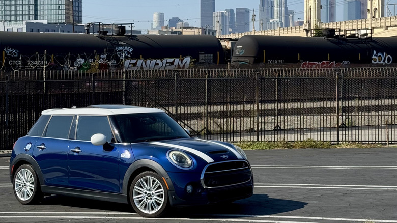 A front three quarters shot of my blue Mini Cooper parked in a parking lot in front of a train and the LA skyline