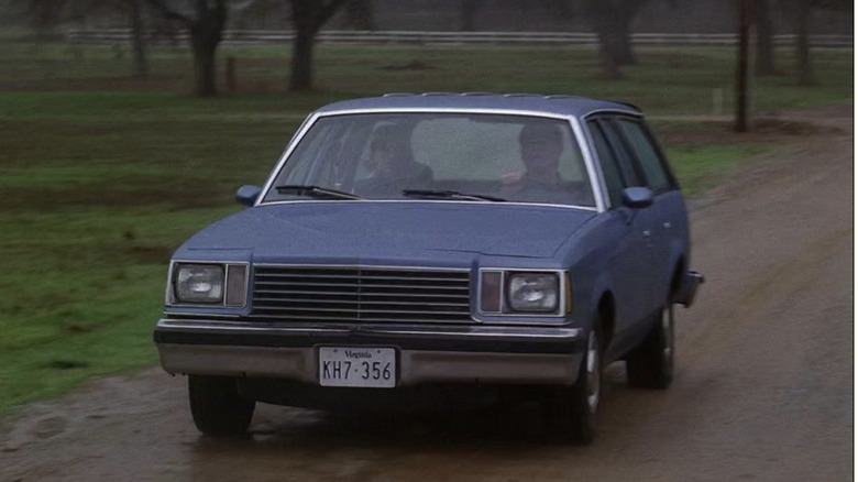 A blue Buick Century Wagon driving down a dirt road