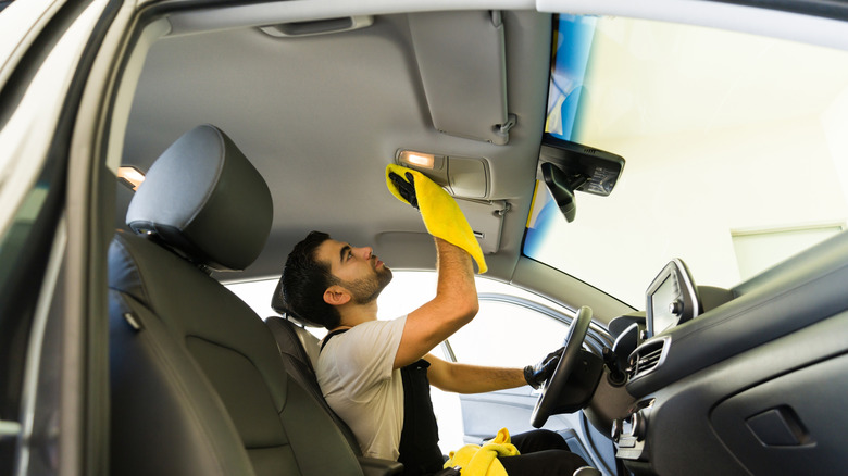 A person using a yellow microfiber towel to clean a car's headliner.