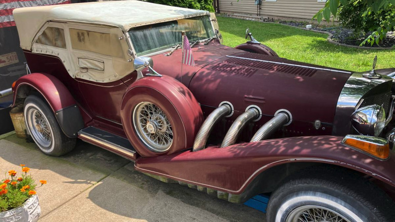 A maroon, sadly dirty, unused 1976 Excalibur Phaeton parked in a driveway.