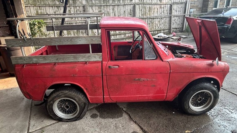 A red Daihatsu Hijet pickup truck with wooden side rails on the bed and its hood open, parked in a suburban driveway.
