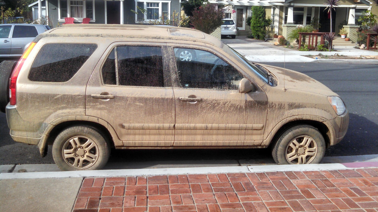 Side view of my brown Honda CR-V covered in dried mud parked on the street next to bricks