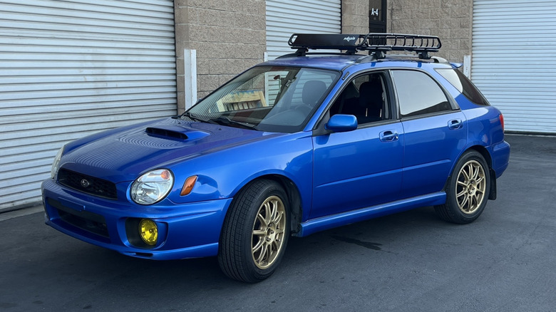 A front three quarters shot of my brother's blue 2003 Subaru WRX wagon with yellow fog lights, gold wheels, and a black roof rack