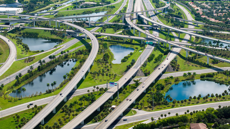An aerial shot of a network of roads and lots of greenery and small lakes around.