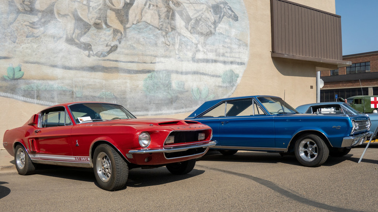 A red Shelby Mustang and a blue 1967 Plymouth GTX in a car show