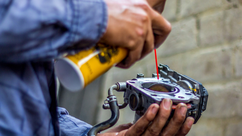 A mechanic using a spray cleaner to clean a car's throttle body