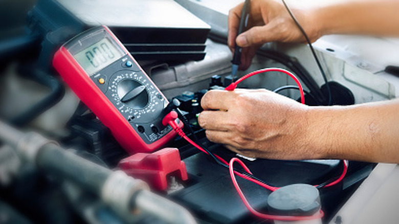 A person checking a car battery's voltage with a multimeter