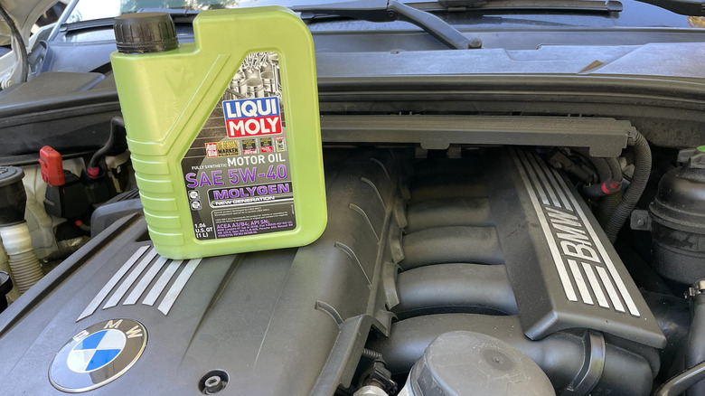 A bottle of engine oil sitting on top of a BMW N52 engine in the bay of a BMW 128i.