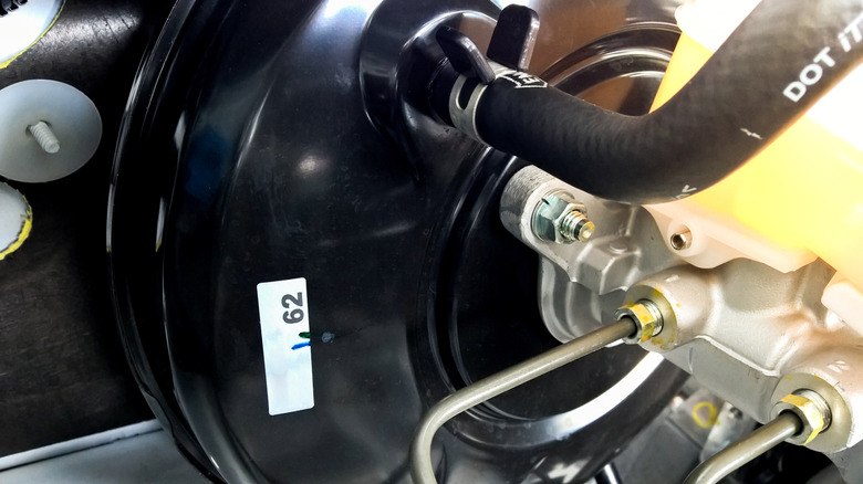 Looking up close at a vacuum brake booster under the hood of a car.