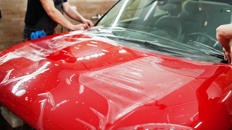 Service workers installing clear PPF on the hood of a red car
