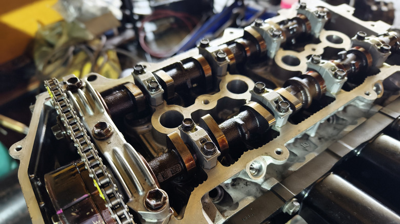 A disassembled car engine showing the dual overhead camshafts on top of the cylinder head