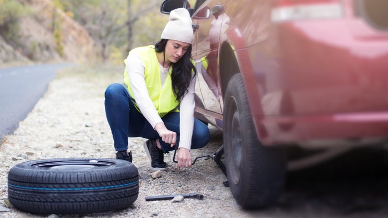 A woman in a white hat and a florescent vest changing a car tire