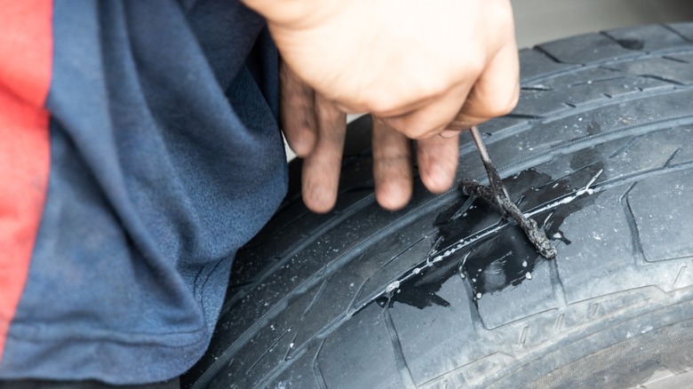A person repairing a car tire with a plug