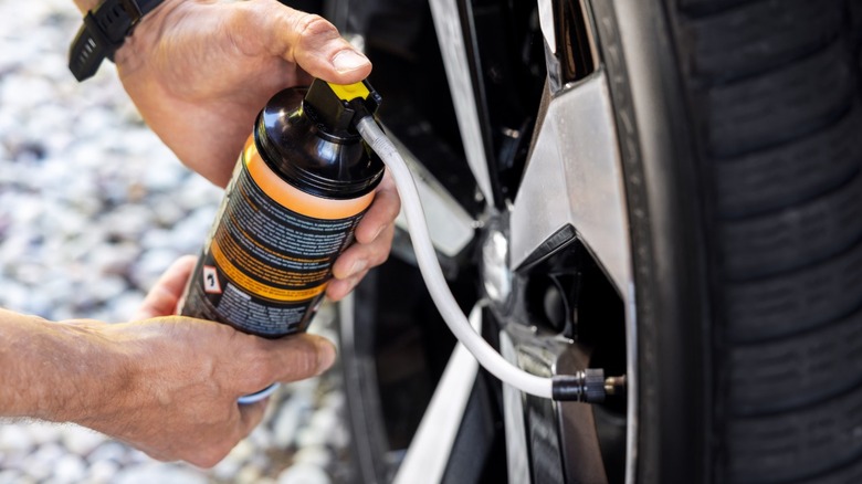 A person using an aerosol can of liquid sealant to fix a flat tire