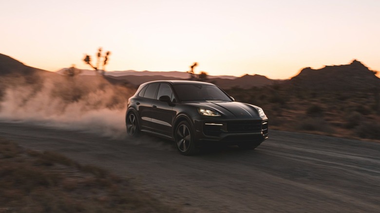 A dark-colored 2026 Porsche Cayenne driving on a dirt road