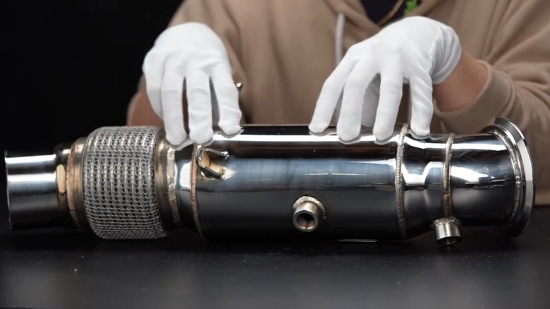 Gloved hands touching an aftermarket catted downpipe for a BMW N55