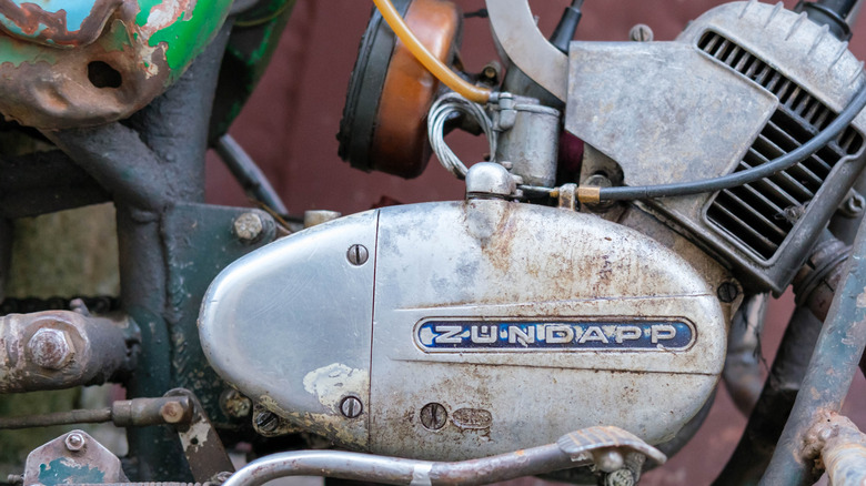 A small Zundapp single-cylinder engine mounted up to a rusty old motorcycle chassis.