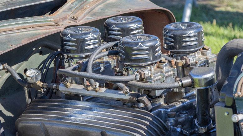 Four carburetors sitting atop a V8 engine inside an old school, patina-rich hotrod.