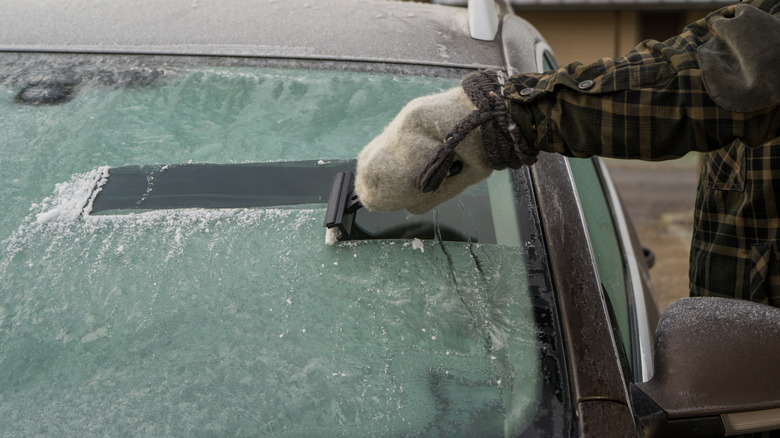 Person scraping ice from a frozen car windshield on a cold winter morning
