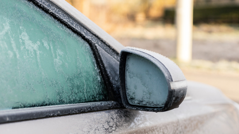 A car sits in a cold morning with its window and side mirror covered in frost