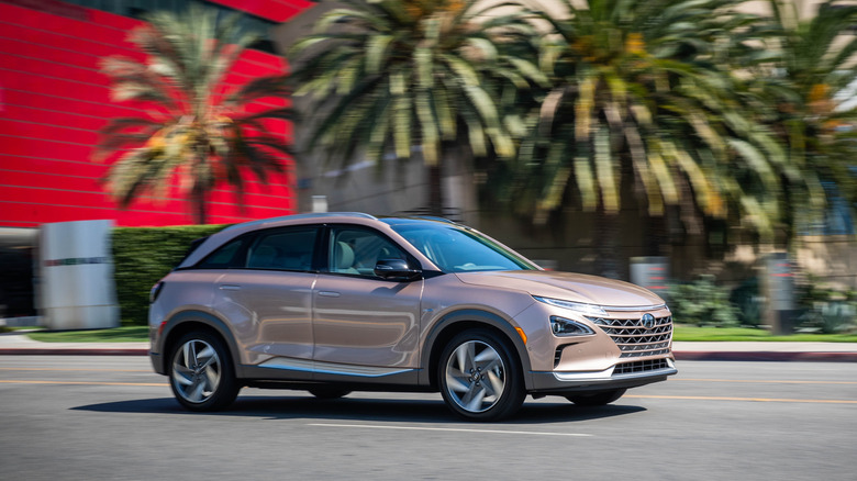 Side view of a rose gold Hyundai Nexo driving past the red part of the Pacific Design Center and some palm trees