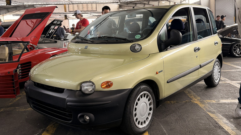 front three quarters shot of a gold Fiat Multipla parked in a building next to a red Ferrari
