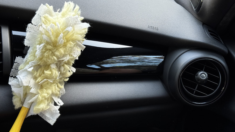 A photo of my yellow Swiffer duster in front of the passenger side dashboard of my Mini's all black interior