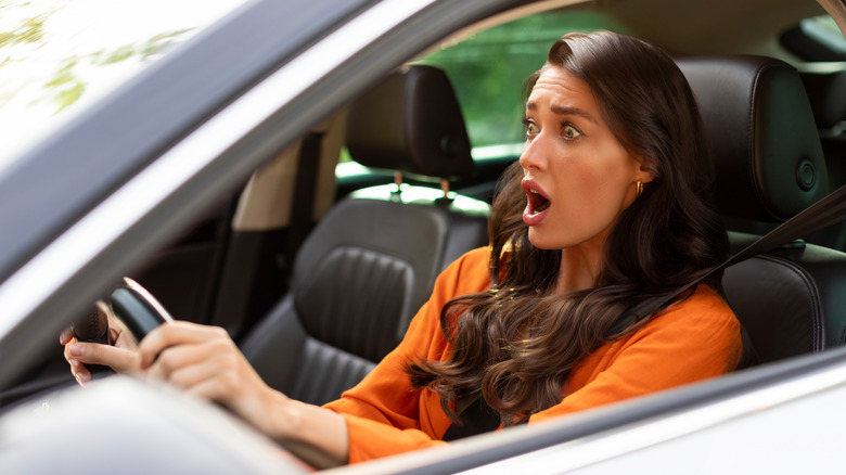 Terrified woman looking with scared expression in front while driving car, having problems or accident on road
