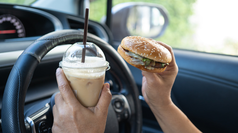 Driver holding a burger and a drink