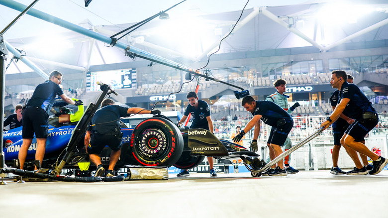a bunch of guys work quickly on an F1 car during a practice pit stop