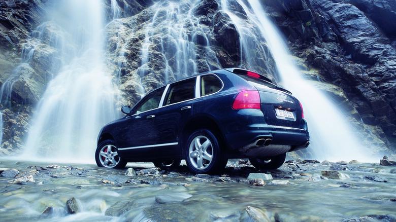 Rear 3/4 view of a blue 2003 Porsche Cayenne Turbo in front of a waterfall