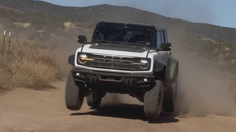 A still image from a video I took of myself in a white Bronco Raptor in the desert right after taking a jump showing my wheels off the ground and a shrub-covered mountain behind me