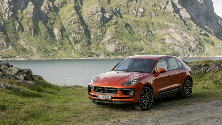 An orange Porsche Macan S parked by a mountain lake