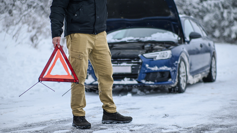 A man places a caution triangle out on the snowy road to indicate his car is disabled