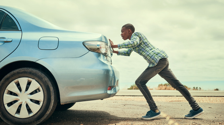Young man pushes a disabled car on the side of the road.